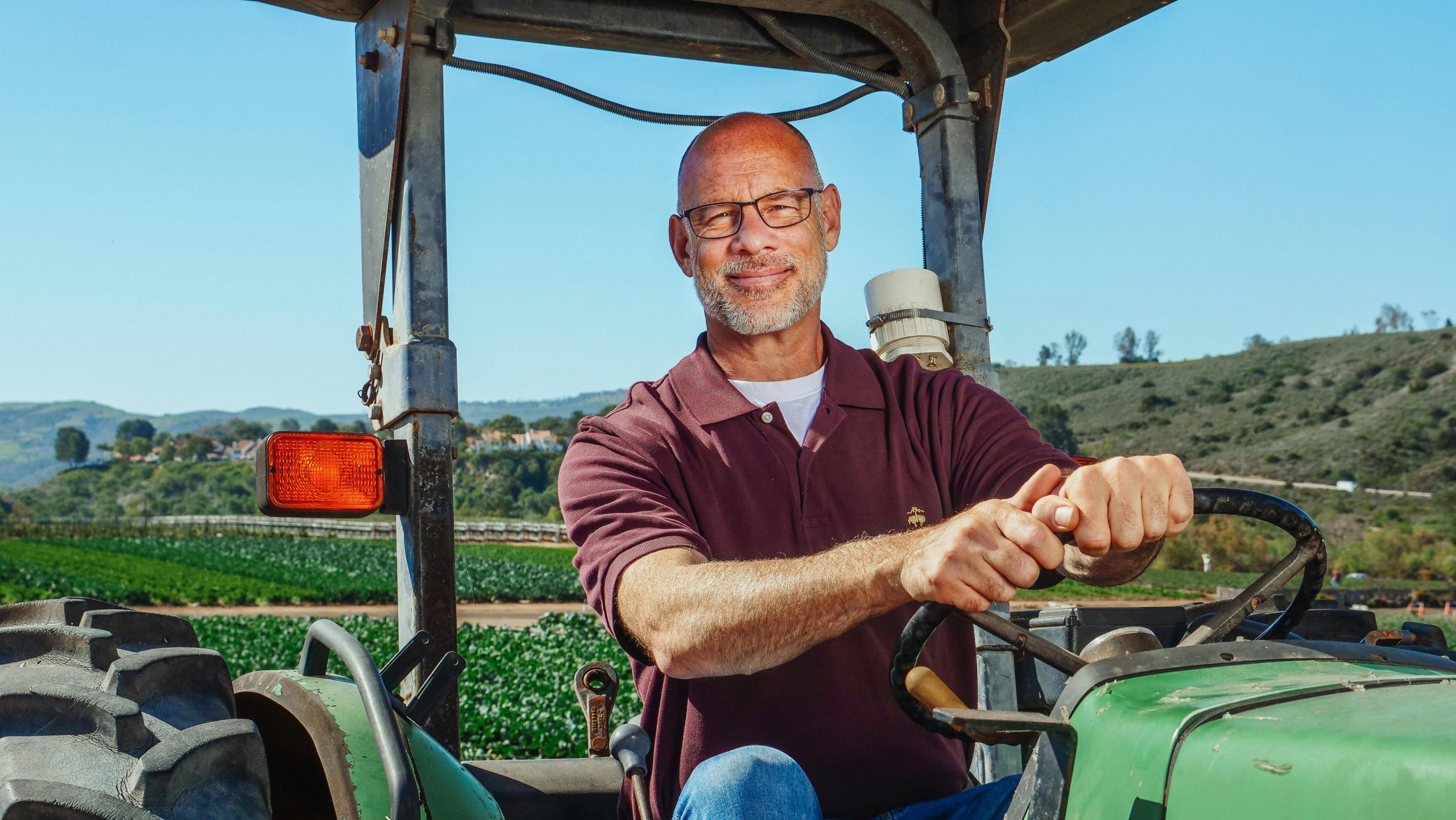 Senior man driving tractor in a sunny farm field, smiling outdoors.