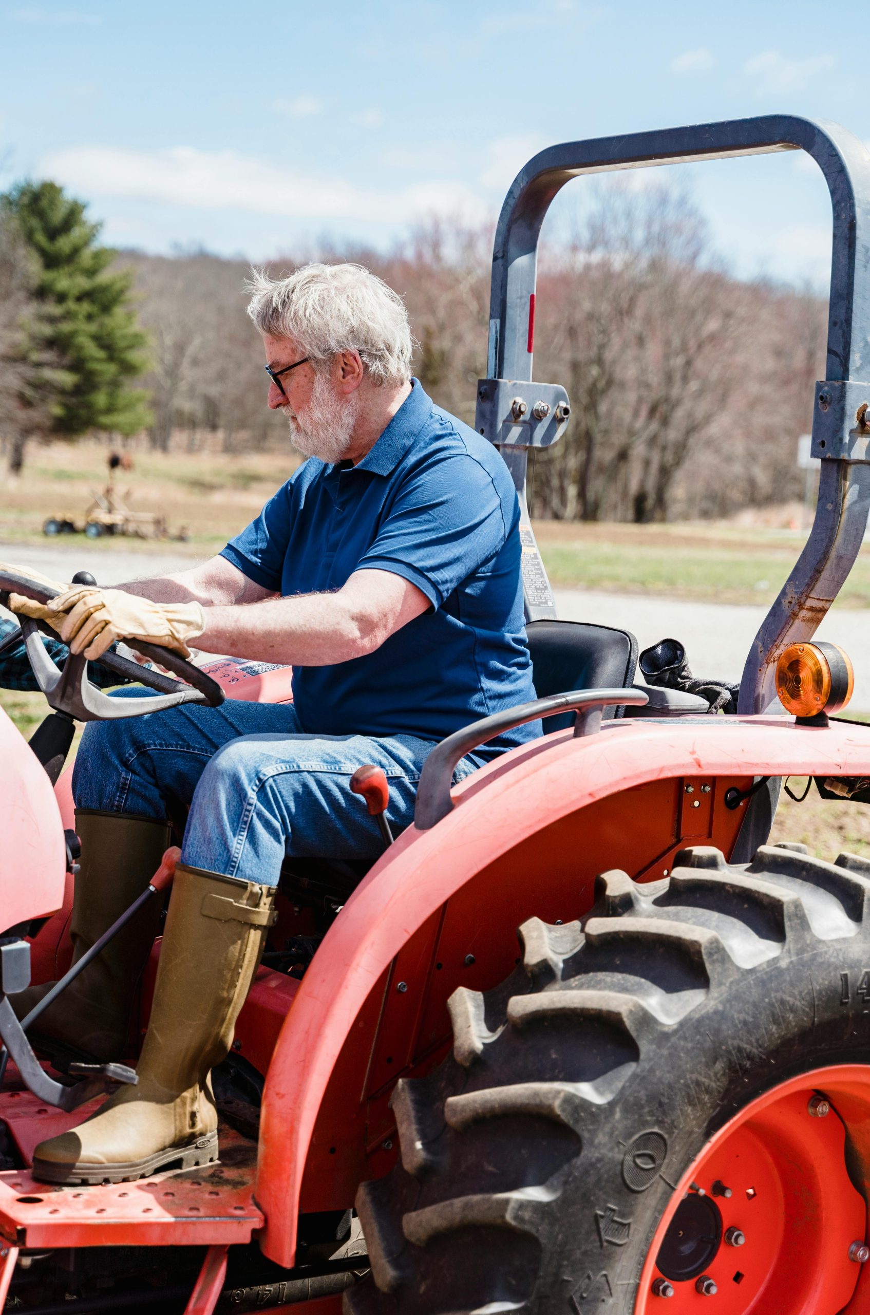 Senior adult man operating a red tractor outdoors in a sunny rural field.